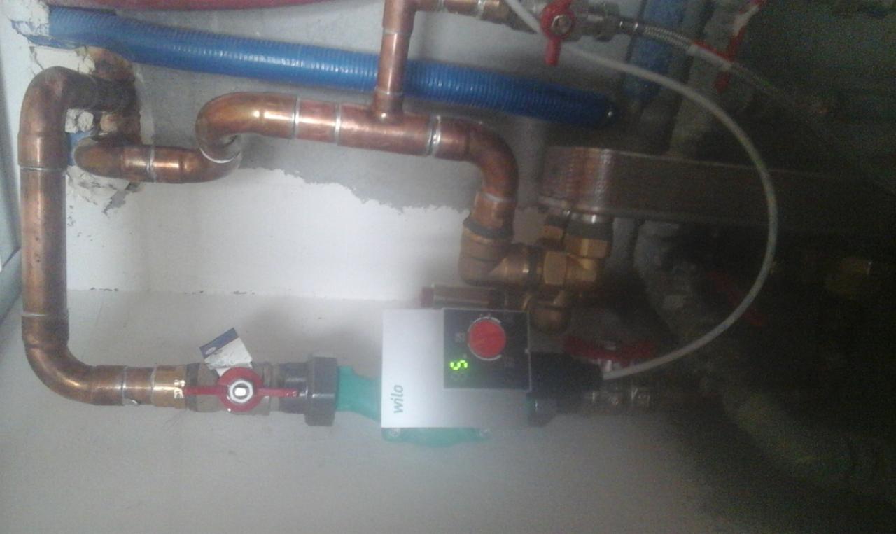 Miedziane rury instalacji grzewczej z zaworami i pompą obiegową Wilo zamontowaną na tle surowej ściany.