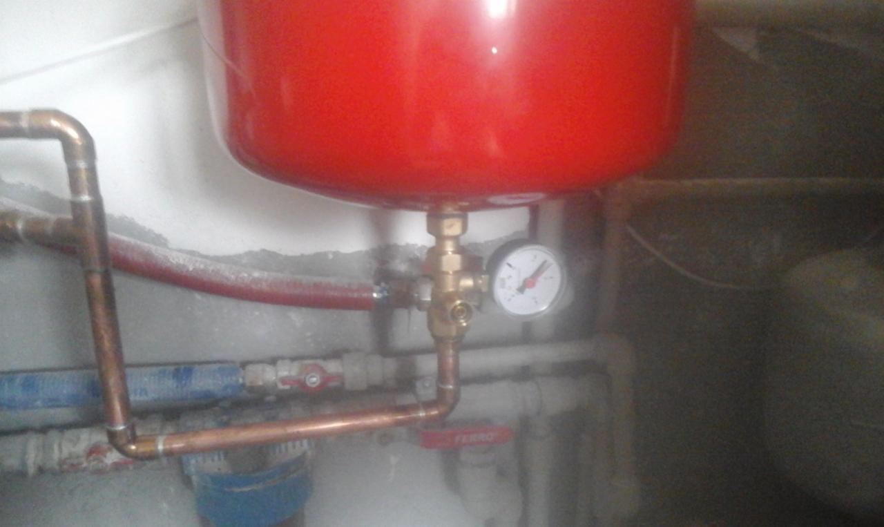 Czerwony zbiornik wyrównawczy w Byczynie, podłączony do instalacji z rur miedzianych i manometrem wskazującym ciśnienie.
