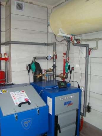 Nowoczesny, niebiesko-szary piec centralnego ogrzewania EKO Plus z podłączonymi rurami i zbiornikiem wyrównawczym, zamontowany w pomieszczeniu z jasnymi, kwadratowymi płytkami.