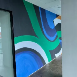 Wnętrze biura z dekoracyjnym malowaniem ścian w kolorach niebieskim, zielonym, białym i czarnym, widok z perspektywy korytarza, podłoga w ciemnej terakocie.