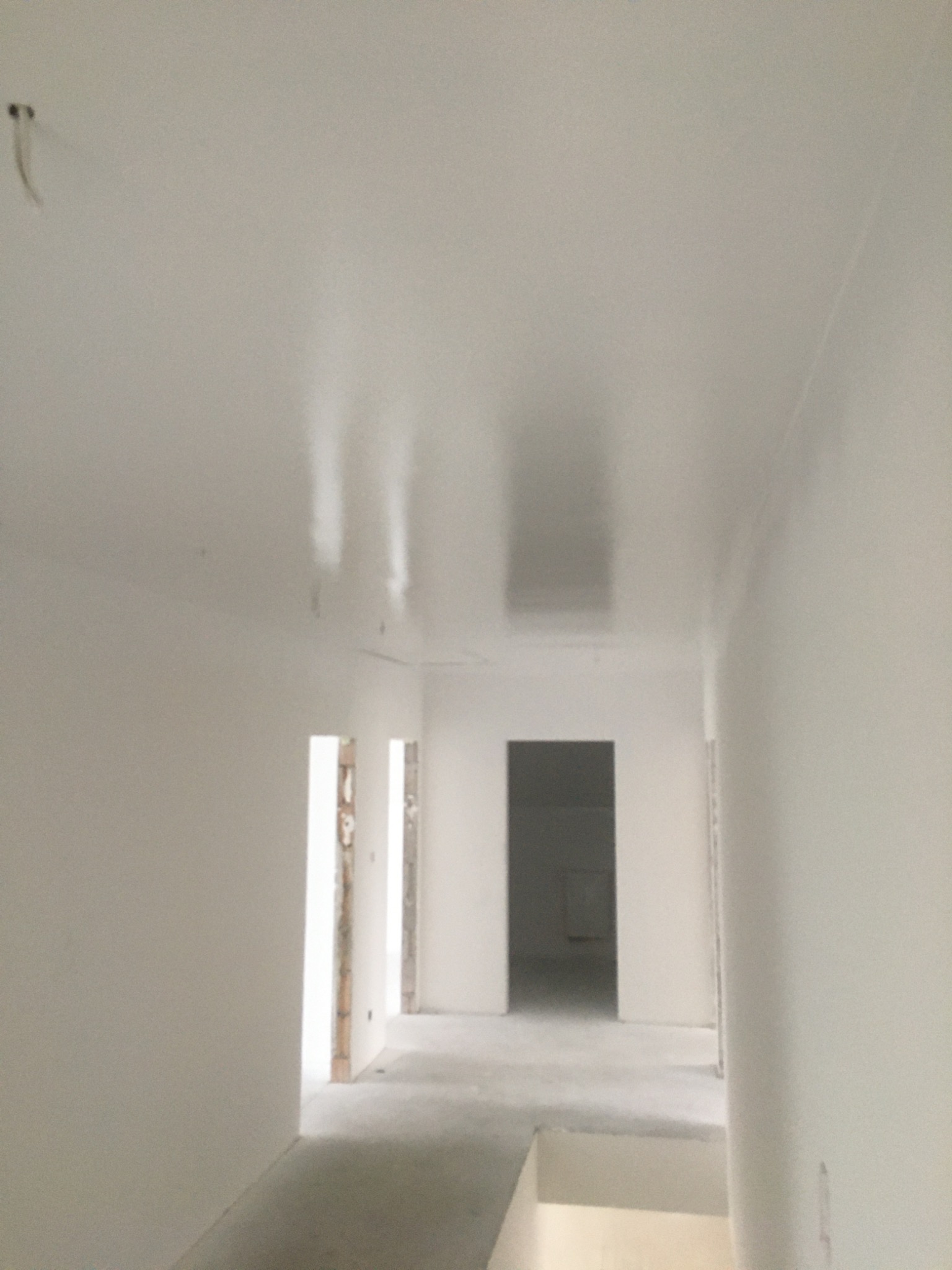 Wnętrze w trakcie wykańczania: świeżo pomalowane na biało ściany i sufit, widoczne otwory drzwiowe z surowymi ościeżnicami, niezagospodarowana przestrzeń.