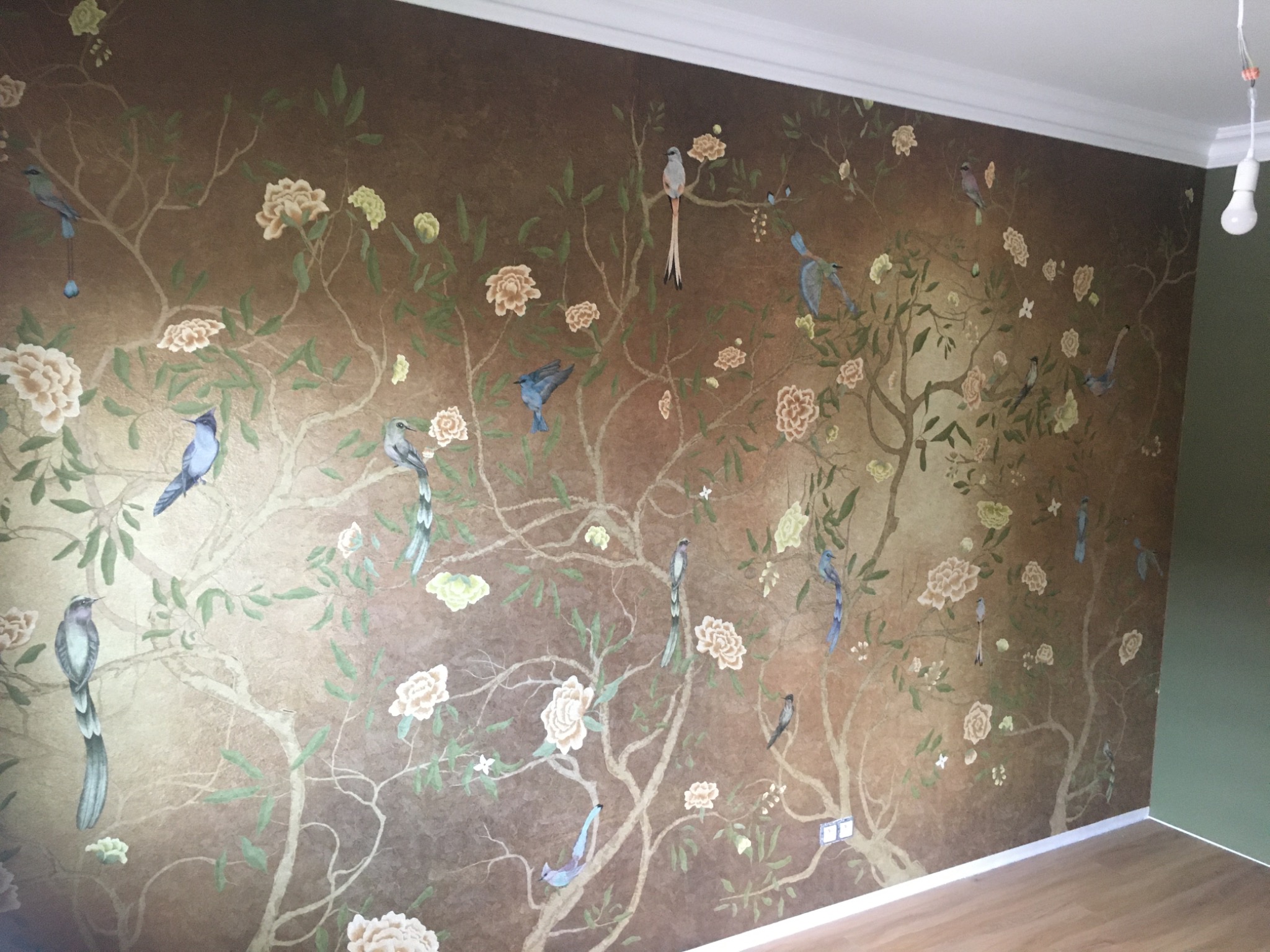 Dekoracyjna ściana w pokoju, pokryta brązową tapetą z motywem drzewa, kwiatów i ptaków w stylu orientalnym.