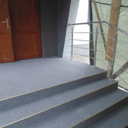 Szare schody zewnętrzne pokryte żywicą z metalową balustradą i drewnianymi drzwiami wejściowymi z boku.