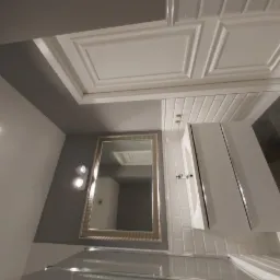 Nowoczesna łazienka z białymi płytkami metra, szafką z umywalką i lustrem w zdobionej ramie, oświetlona lampami ściennymi.