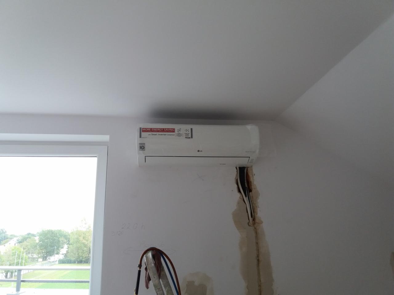 Montaż klimatyzatora LG na ścianie w pomieszczeniu, widoczne ślady po instalacji przewodów, drabina oparta o ścianę, okno w tle.