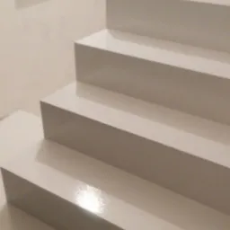 Białe, minimalistyczne schody wewnętrzne pokryte błyszczącą powłoką, widoczne z dołu, z oknem w tle, z logo firmy w rogu.