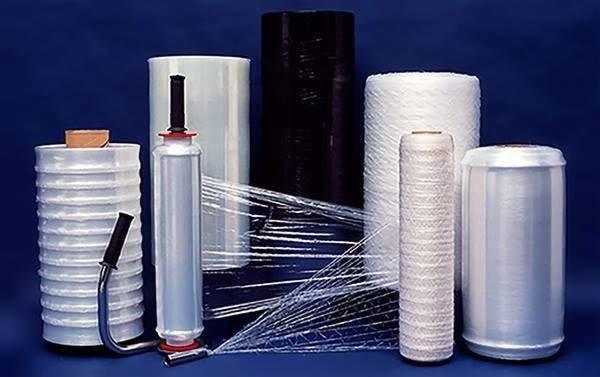 Różne rodzaje folii stretch w rolkach: przezroczysta, czarna, biała, z aplikatorem ręcznym, na ciemnoniebieskim tle.