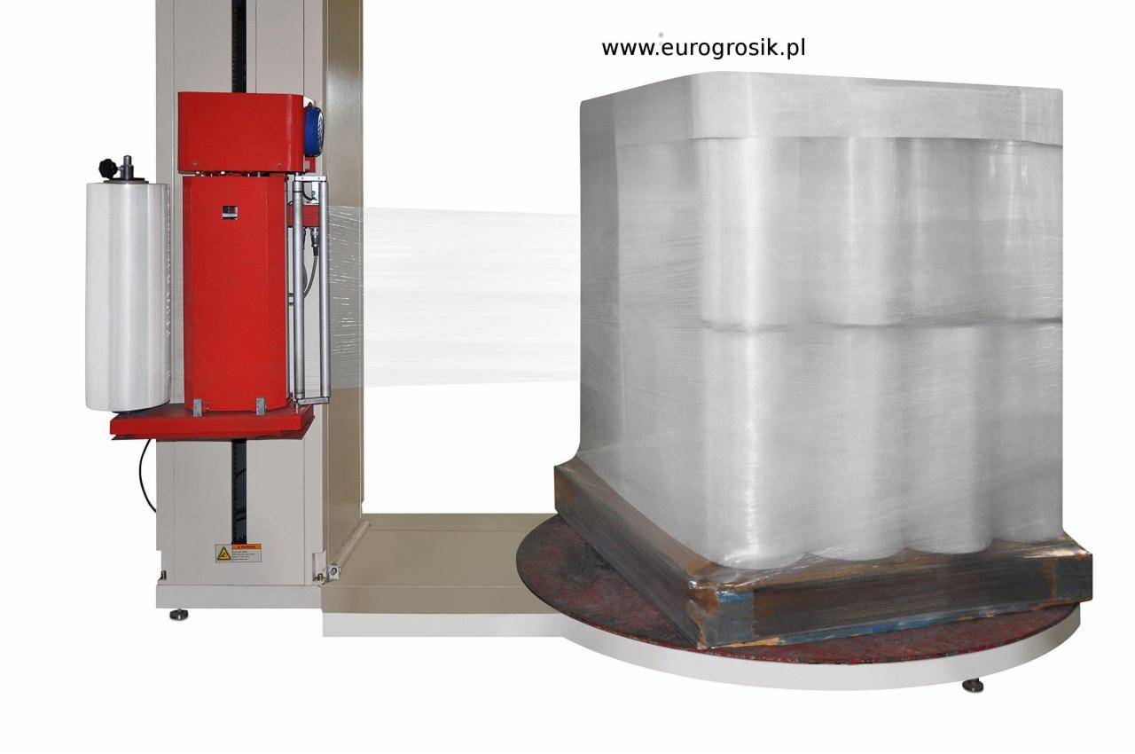 Automatyczna owijarka palet z czerwonym panelem sterowania, owijająca transparentną folią paletę z towarem, widoczny adres strony internetowej producenta w prawym górnym rogu.
