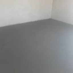 Świeżo wylana, gładka, szara posadzka w pustym, jasnym pomieszczeniu z białymi ścianami. Widoczne delikatne refleksy światła na powierzchni.