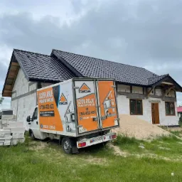 Samochód dostawczy z reklamą ocieplania pianą PUR i wełną na tle domu w trakcie budowy z widocznym dachem i stertą piasku.