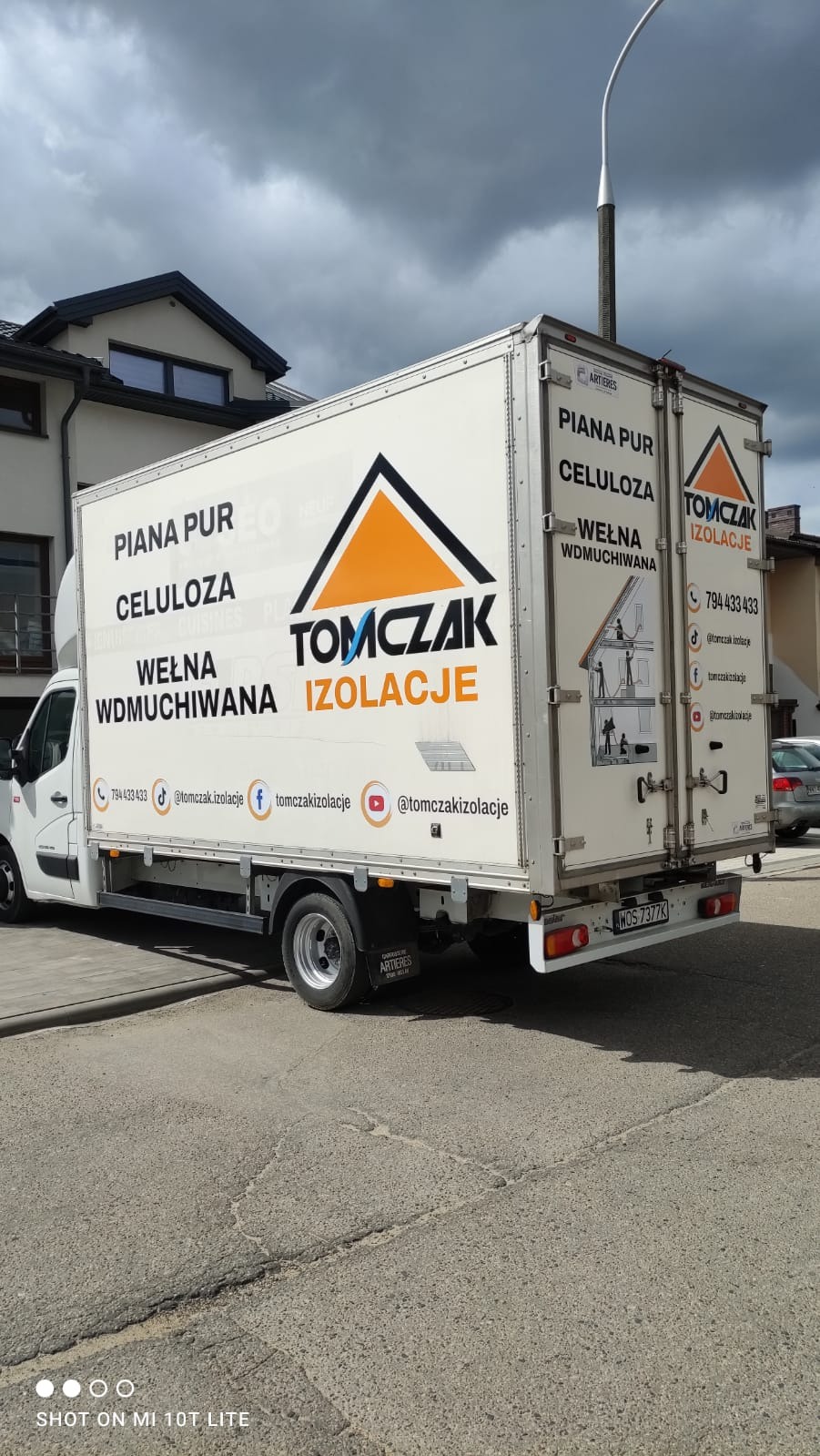 Pojazd dostawczy z reklamą firmy Tomczak Izolacje, oferującej ocieplanie pianą PUR, celulozą i wełną wdmuchiwaną. Widoczne dane kontaktowe i logo firmy.