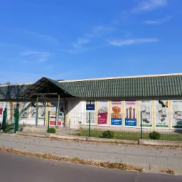 Budynek sklepu z materiałami budowlanymi z reklamami produktów na elewacji, widok z zewnątrz w słoneczny dzień.