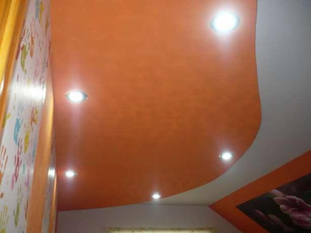 Pomarańczowy, podwieszany sufit z wbudowanymi punktowymi lampami, ściana z tapetą w dziecięce wzory, fragment dekoru ściennego w rogu.