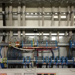 Otwarta szafa elektryczna z licznymi przewodami, listwami zaciskowymi i zabezpieczeniami, uporządkowane okablowanie wewnątrz szyny montażowej.