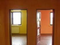 Widok przez dwa otwarte przejścia drzwiowe: po lewej pokój z żółtymi ścianami i grzejnikiem pod oknem, po prawej pokój z pomarańczowymi ścianami i częściowo otwartymi drzwiami.