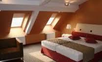 Pomarańczowe wnętrze sypialni na poddaszu z ukośnymi ścianami, dwoma oknami dachowymi, łóżkiem z czerwonymi akcentami i beżowym dywanem.