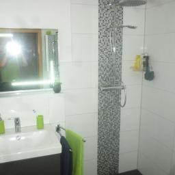 Usługi Remontowo-Wykończeniowe Tomasz Stachowicz - Nowoczesna łazienka z białą glazurą, kabiną prysznicową typu walk-in z deszczownicą i mozaikowym pasem, umywalką wpuszczaną w ciemną szafkę oraz zielonymi akcentami w postaci kubków na szczoteczki...