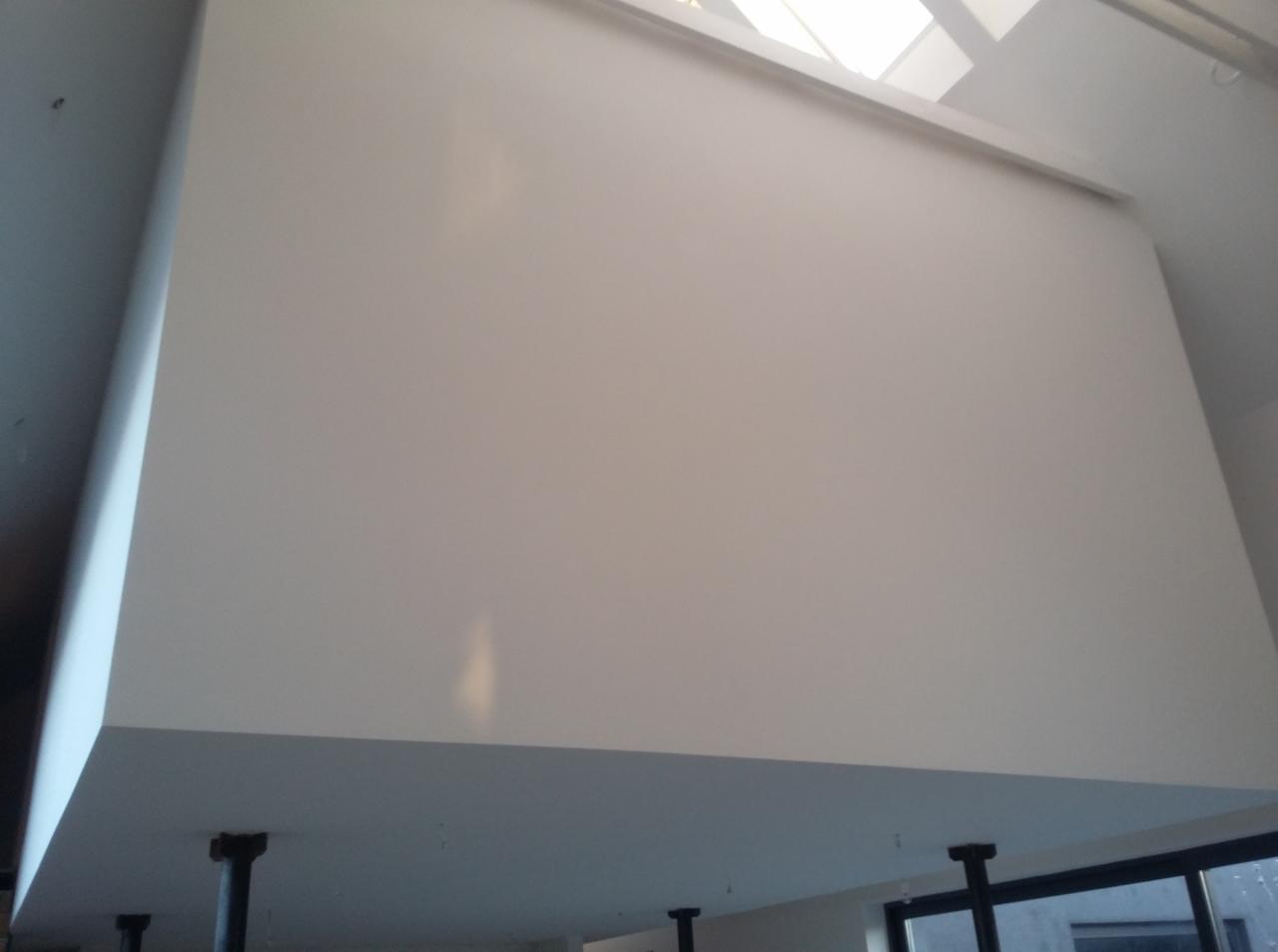 Wysoka, gładka, biała ściana po tynkowaniu maszynowym, widok z dołu, fragment okna w tle.