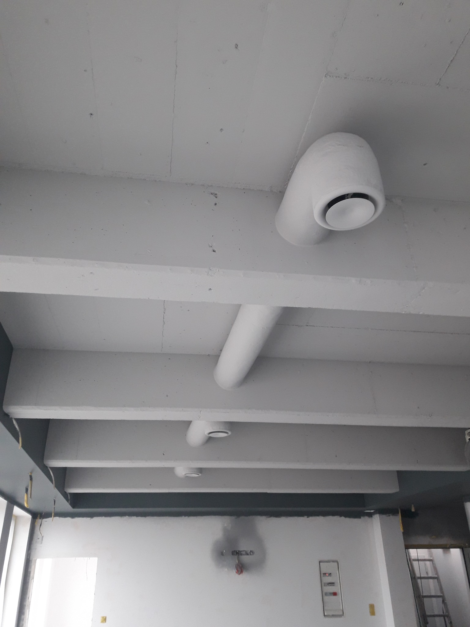 Białe, okrągłe nawiewniki klimatyzacji zamontowane na betonowym suficie w surowym wnętrzu biurowym.