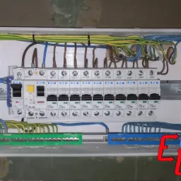 Rozdzielnica elektryczna marki Eaton w plastikowej obudowie, z widocznymi przewodami w kolorach: zielono-ż&oacute;łtym, niebieskim i brązowym, zabezpieczonymi czarnymi opaskami zaciskowymi, zamontowana...