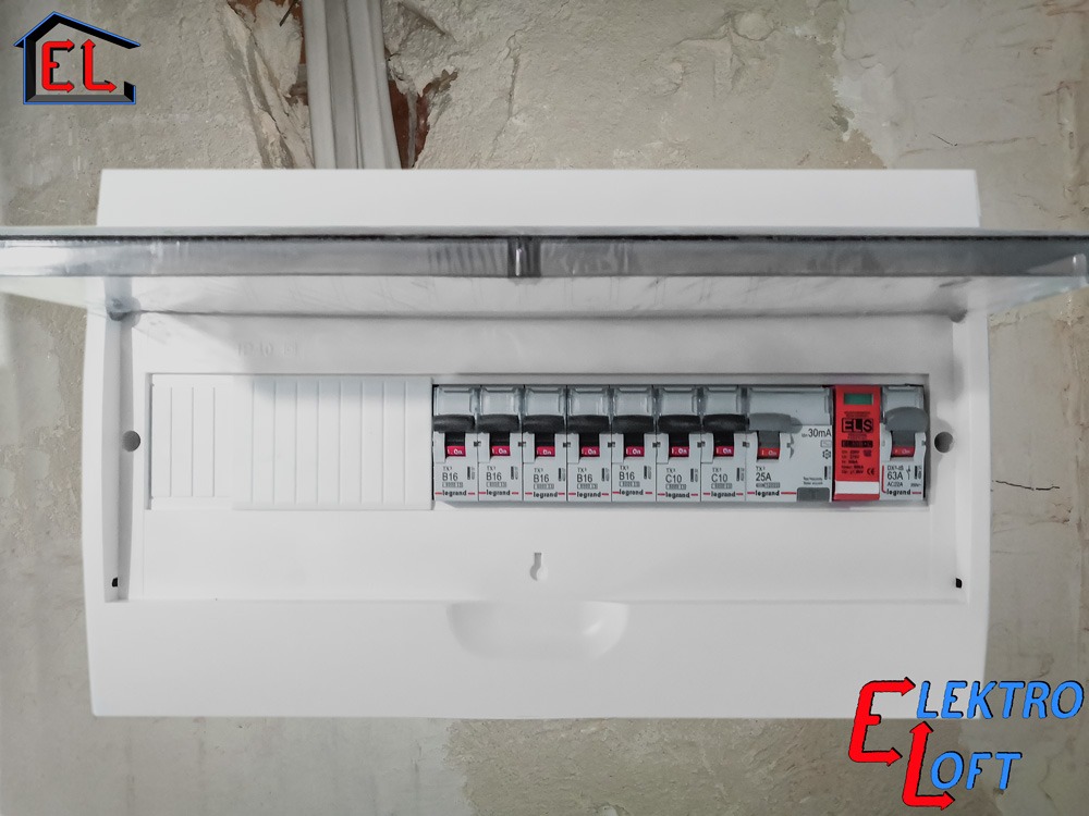 Otwarta, biała skrzynka rozdzielcza z bezpiecznikami Legrand na ścianie z surowego betonu. Widoczne oznaczenia bezpieczników i logo ELS.