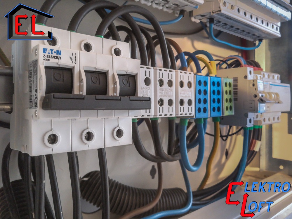 Rozdzielnica elektryczna z zamontowanymi bezpiecznikami EATON i listwami zaciskowymi, widoczne kable w różnych kolorach, ułożone wewnątrz metalowej obudowy.