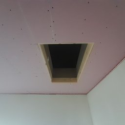 remonty wykończenia wnetrz - Sufit z różowej płyty, częściowo zamontowany z otworem inspekcyjnym obramowanym drewnem, widoczne ślady po wkrętach i łączenia płyt.