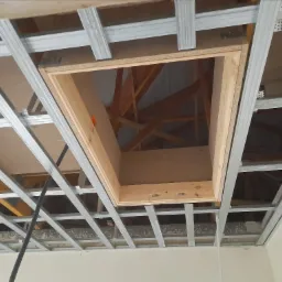 Stelaż sufitowy z zamontowanym drewnianym otworem rewizyjnym, widoczne elementy konstrukcji dachu.