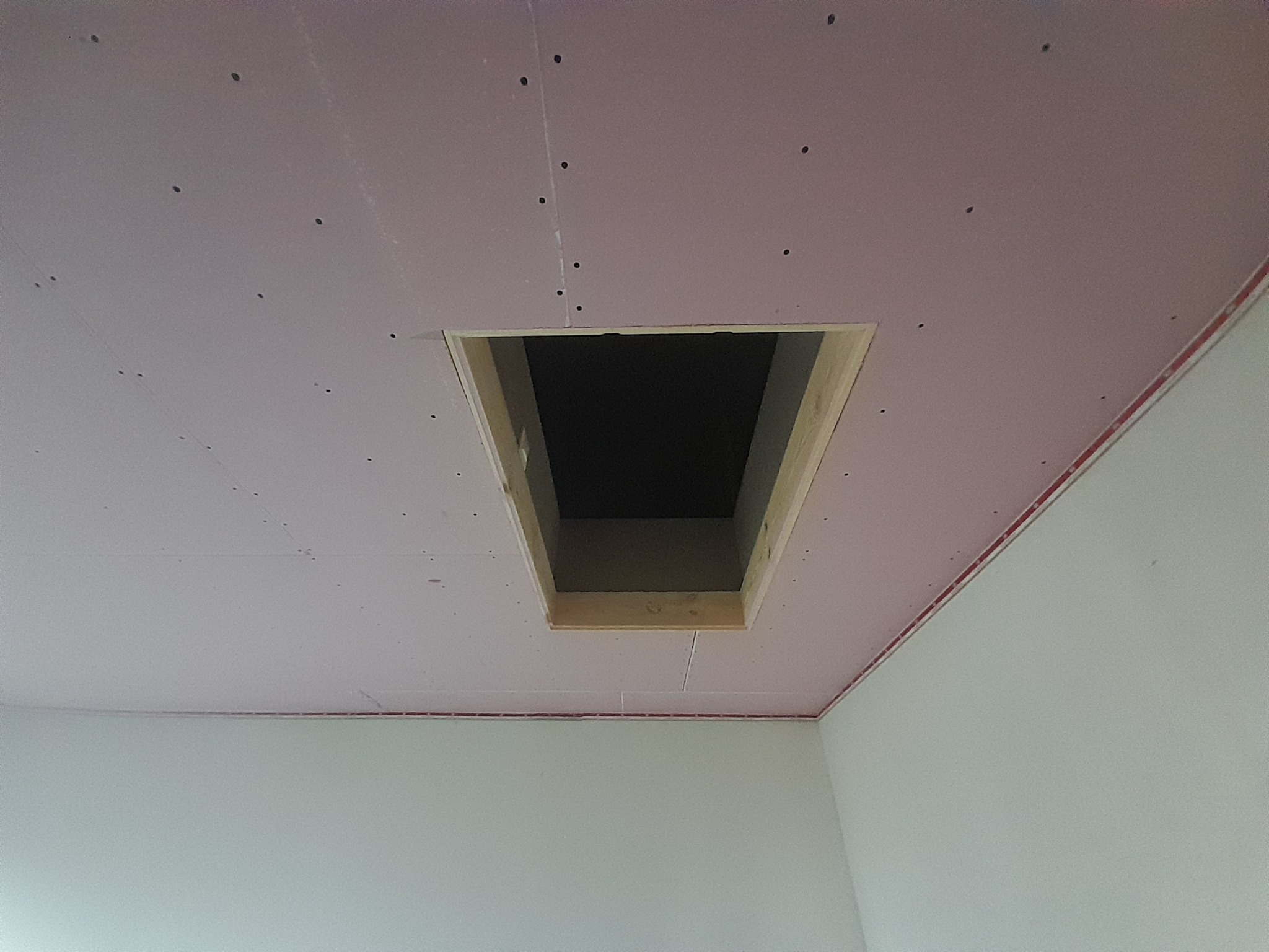Sufit z różowej płyty, częściowo zamontowany z otworem inspekcyjnym obramowanym drewnem, widoczne ślady po wkrętach i łączenia płyt.