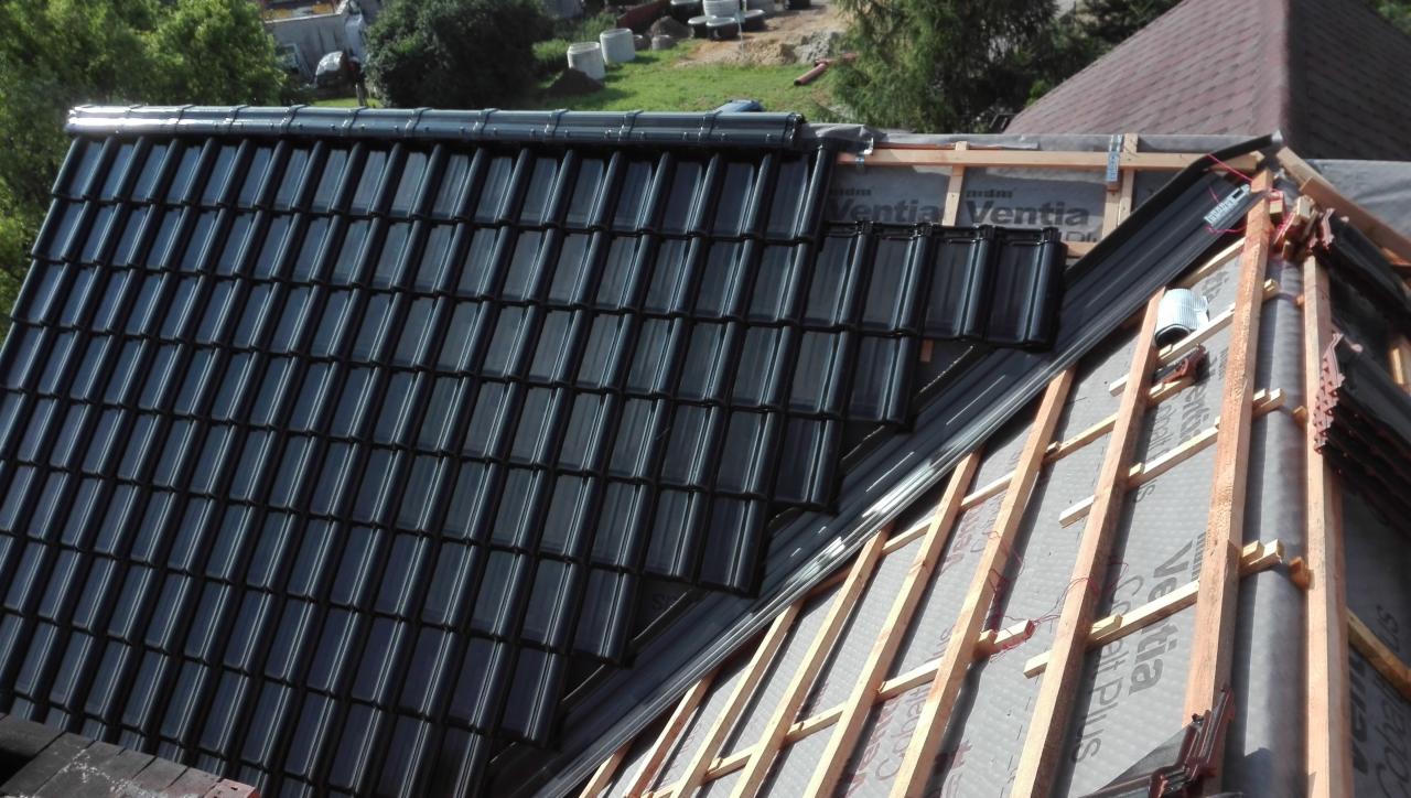 Układanie czarnej dachówki ceramicznej na konstrukcji dachu z membraną w tle zieleni.