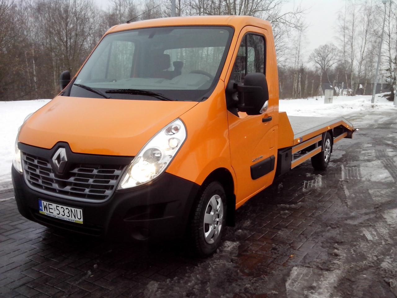 Pomarańczowa laweta Renault Master na mokrym bruku w zimowej scenerii z odśnieżonym poboczem.