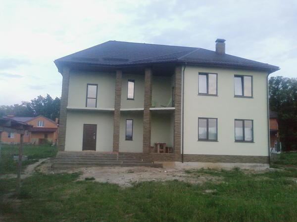 Dwukondygnacyjny dom z jasną elewacją i schodami wejściowymi wyłożonymi kostką brukową, widok z zewnątrz.