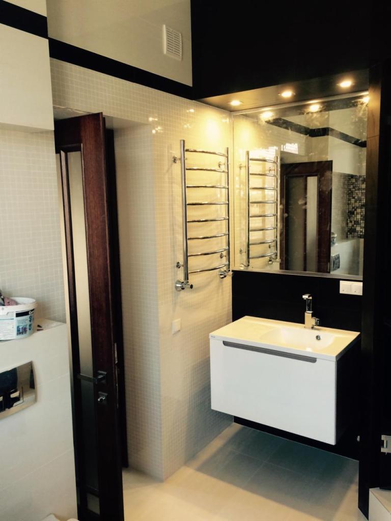 Nowoczesna łazienka z białymi płytkami mozaikowymi, podświetlanym lustrem, wiszącą szafką z umywalką i grzejnikiem drabinkowym.