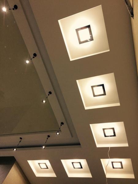 Sufit z wbudowanymi kwadratowymi lampami LED, oświetlenie punktowe na podwieszanym suficie, ciepłe światło.