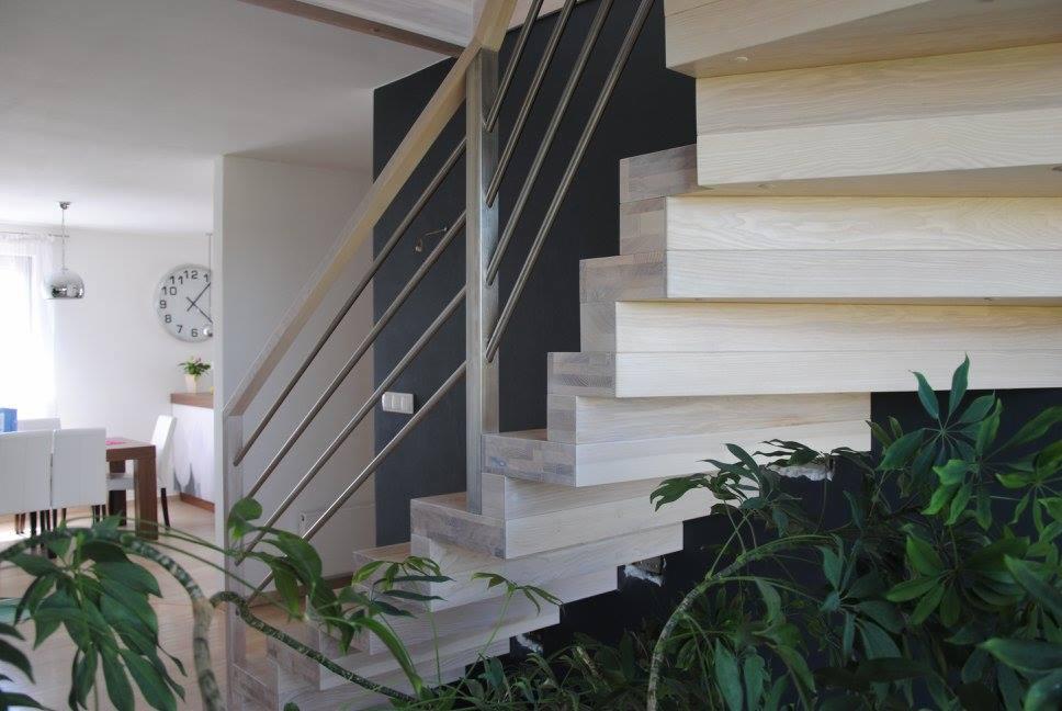 Nowoczesne schody z jasnego drewna z metalową balustradą, widok z dołu, z roślinami w tle, minimalistyczny design.