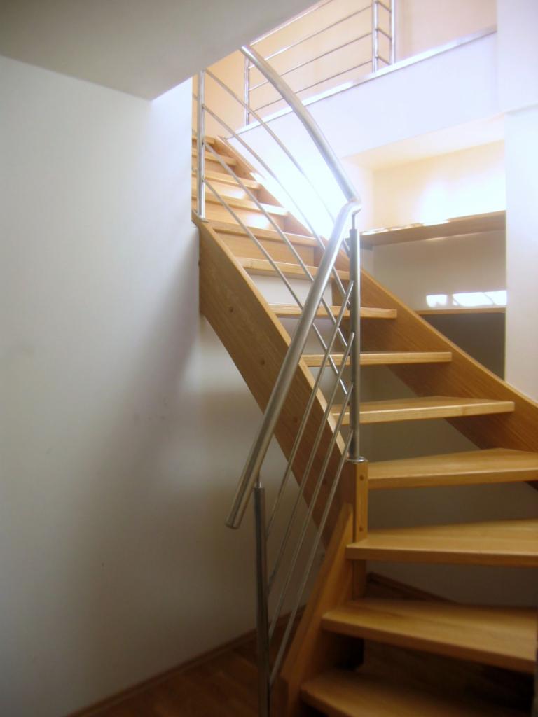 Klatka schodowa z jasnego drewna z metalową balustradą w nowoczesnym stylu, widok z dołu, jasne wnętrze.