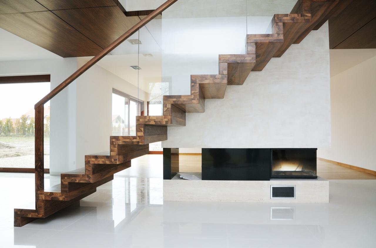 Nowoczesne schody wspornikowe z drewna klejonego, z balustradą ze szkła, w jasnym wnętrzu z kominkiem.