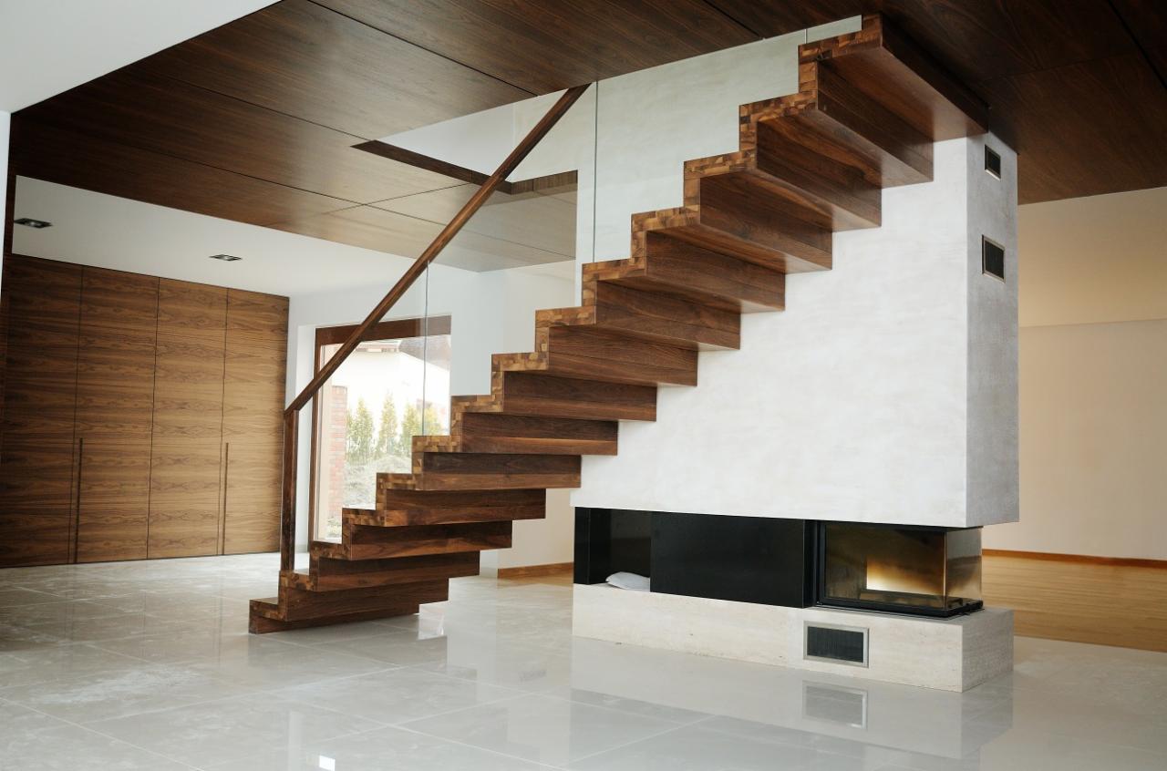 Nowoczesne, samonośne schody drewniane z balustradą ze szkła hartowanego, wkomponowane w minimalistyczny wystrój wnętrza z drewnianym sufitem i kominkiem.