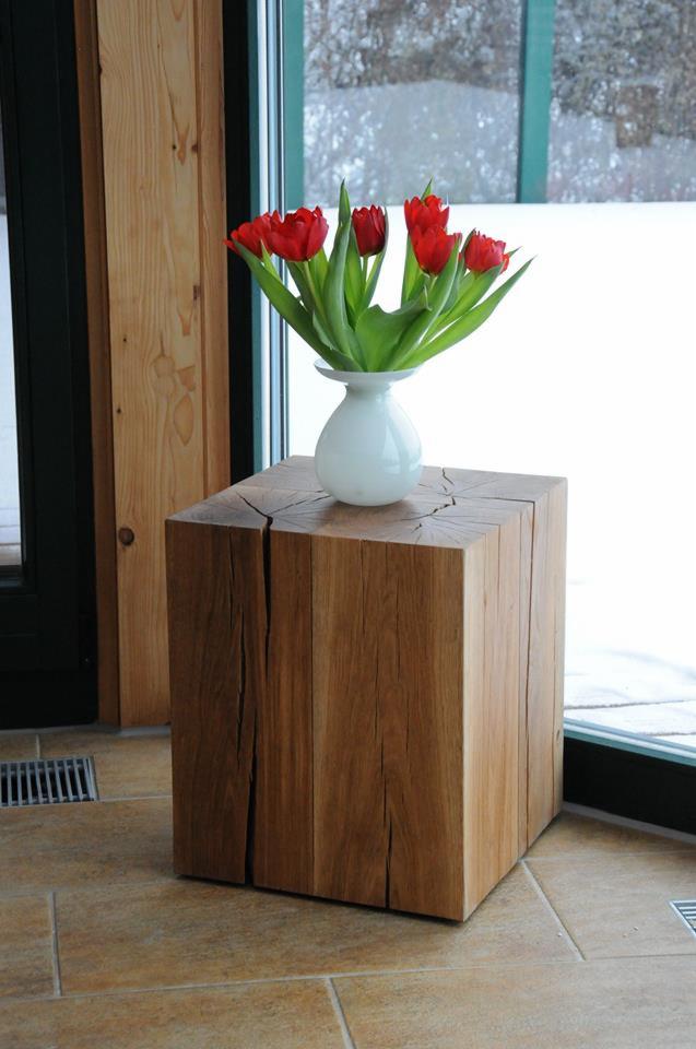 Drewniany, sześcienny stolik nocny z widocznymi pęknięciami, na którym stoi biały wazon z czerwonymi tulipanami, na tle okna z widokiem na zaśnieżony krajobraz.