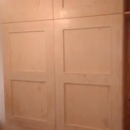 Jasna, drewniana szafa wnękowa z panelowymi drzwiami, widoczna częściowo półka po prawej stronie, ujęcie z dołu.