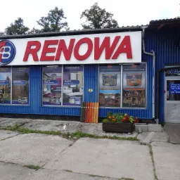 Fasada sklepu z materiałami budowlanymi Renowa z logo AB, prezentacja bejc i lakierów na wystawie, paleta kolorów, donica z kwiatami i biały kot siedzący przed wejściem.