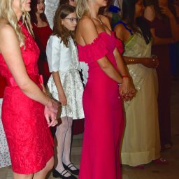 Zbigniew Płotka - e-foto-art - Grupa eleganckich kobiet i dziewczynka w wieczorowych strojach, w tym fuksjowej sukni i sari, stojących w rzędzie podczas uroczystości w stylowym wnętrzu.