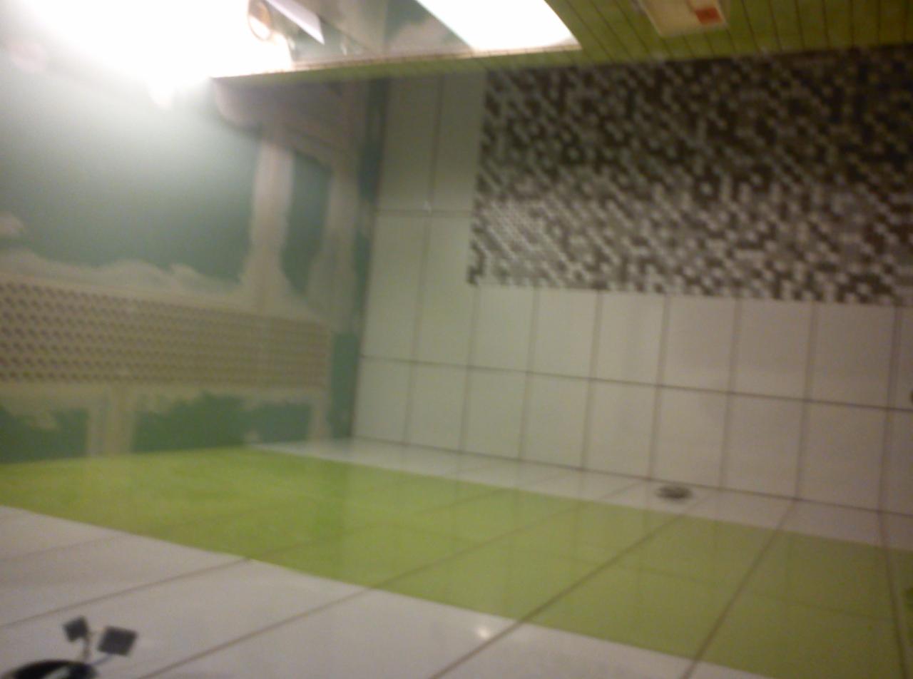 Wnętrze łazienki w trakcie remontu: położone płytki podłogowe w odcieniach zieleni i bieli, częściowo wykończona ściana z białych płytek oraz dekoracyjna mozaika na górze, widoczne ślady po pracach...