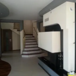 Nowoczesny salon z kominkiem o geometrycznej bryle, widoczne schody z drewnianymi stopniami i metalową balustradą oraz dekoracyjna ściana z telewizorem.