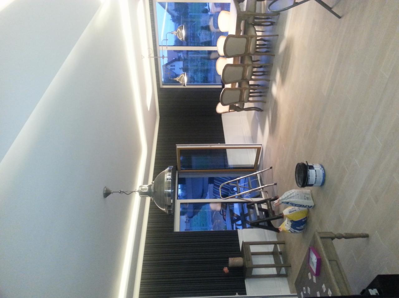 Nowoczesne wnętrze w trakcie wykańczania: widoczny fragment sufitu z oświetleniem LED, ściana z ciemnymi panelami, otwarte okno, drabina, wiadro z farbą i worki z materiałami budowlanymi...