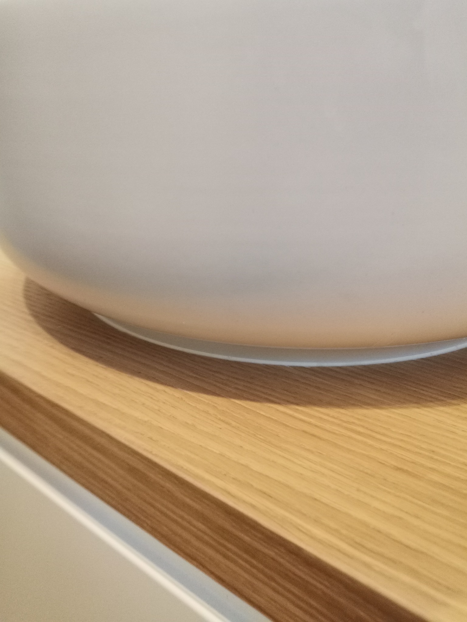 Fragment blatu z jasnego drewna z widocznym cieniem okrągłego przedmiotu, prawdopodobnie miski lub zlewu.