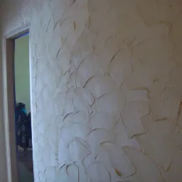 Ściana z dekoracyjną fakturą, nałożona szpachlą w nieregularne, półokrągłe wzory, widoczny fragment ościeżnicy drzwi.