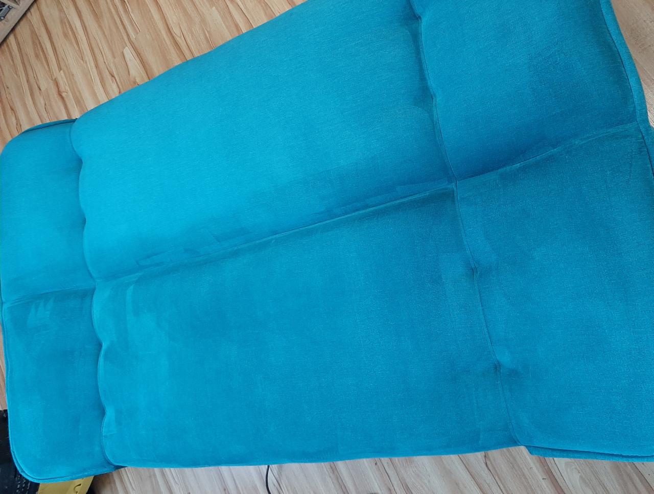 Turkusowa sofa z widocznym efektem czyszczenia, gdzie jedna część jest wyraźnie jaśniejsza od drugiej.