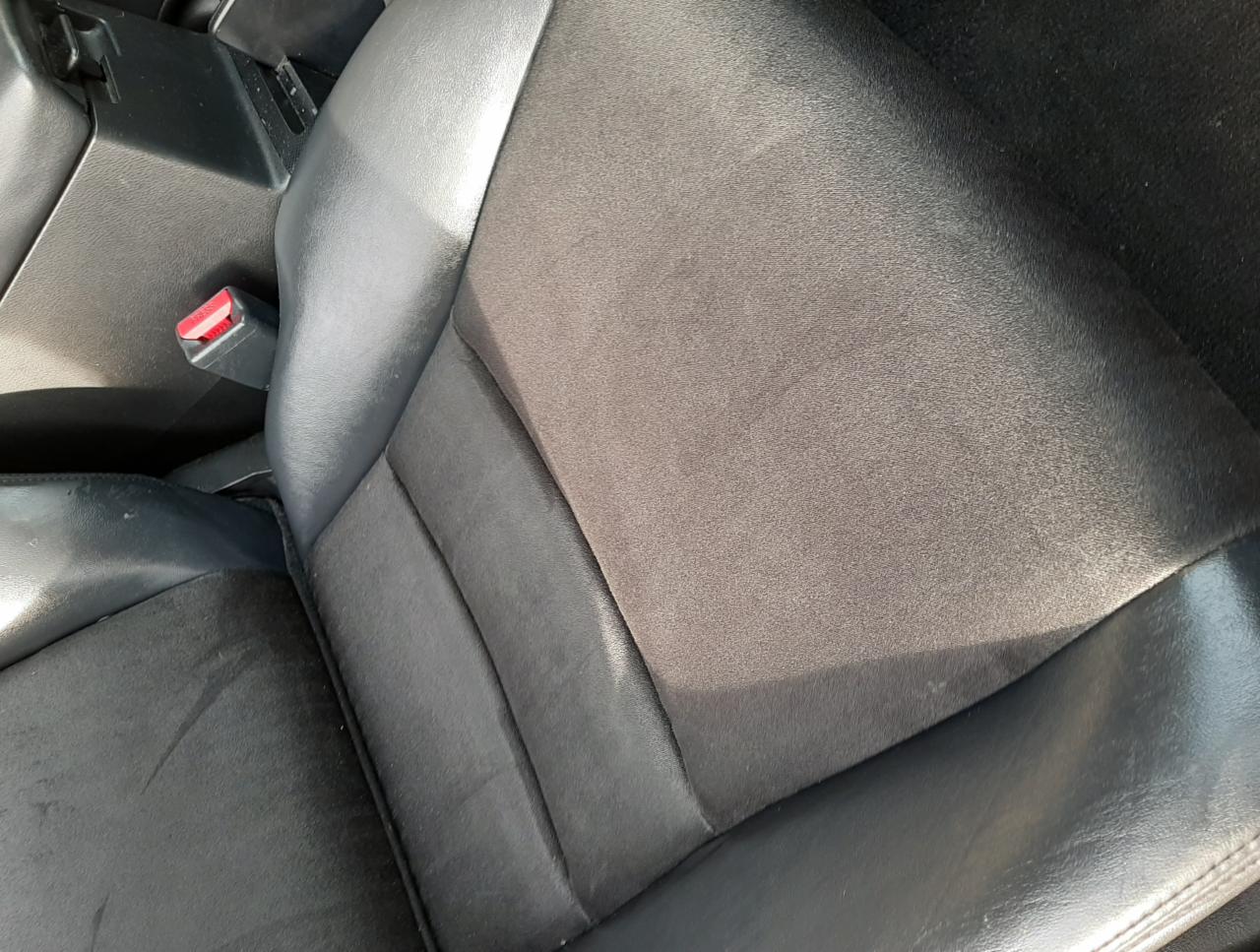 Czarny, materiałowy fotel samochodowy z widocznymi śladami użytkowania i zaciekami, obok zapięcie pasa bezpieczeństwa.