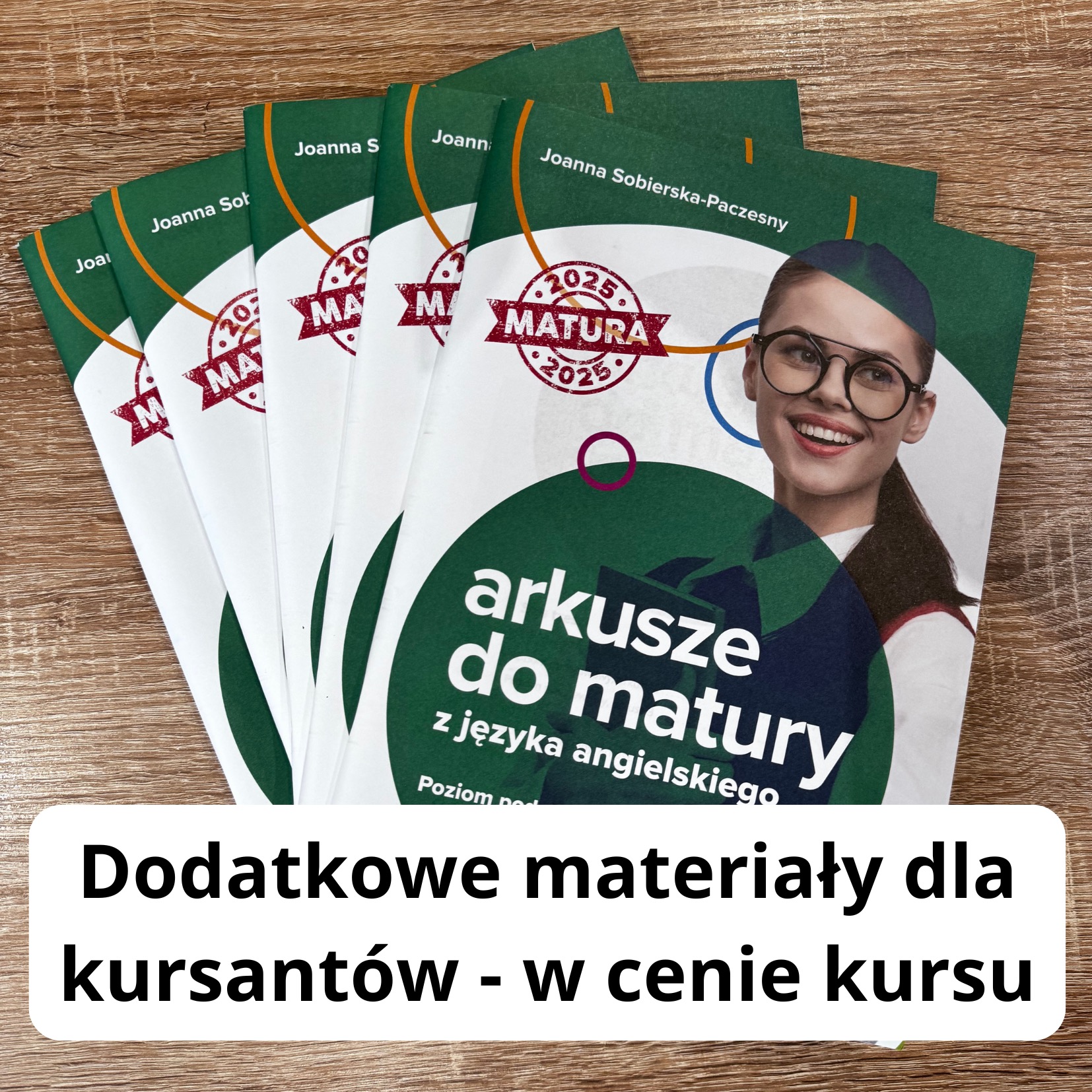 Stos zielonych broszur z napisem 'arkusze do matury z języka angielskiego' na drewnianym stole, widoczna uśmiechnięta kobieta w okularach na okładce.